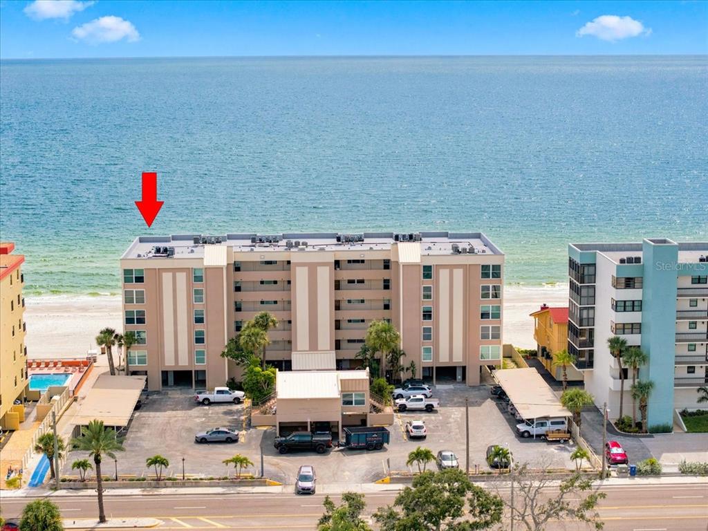 An aerial view of a multi-story beachfront condominium building with a parking lot in front — 14800 GULF BOULEVARD UNIT 207, MADEIRA BEACH, FL