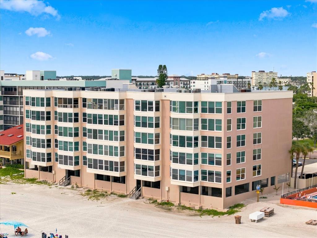An exterior view of a multi-story beachfront condominium building with large windows and sandy surroundings — 14800 GULF BOULEVARD UNIT 207, MADEIRA BEACH, FL