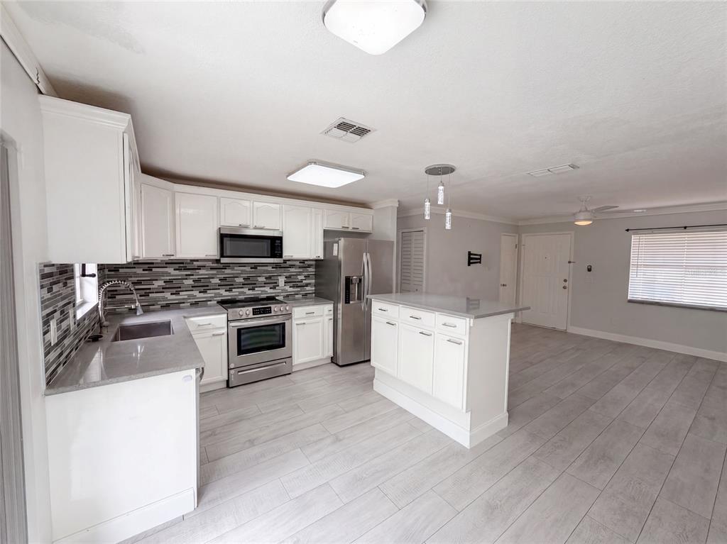 A kitchen with white cabinets, stainless steel appliances, a center island, and light wood flooring — 976 LISKEARD AVENUE, ORANGE CITY, FL