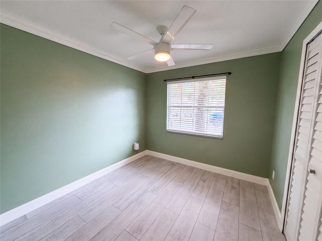 An empty bedroom features sage green walls, light wood-look tile flooring, and a ceiling fan — 976 LISKEARD AVENUE, ORANGE CITY, FL