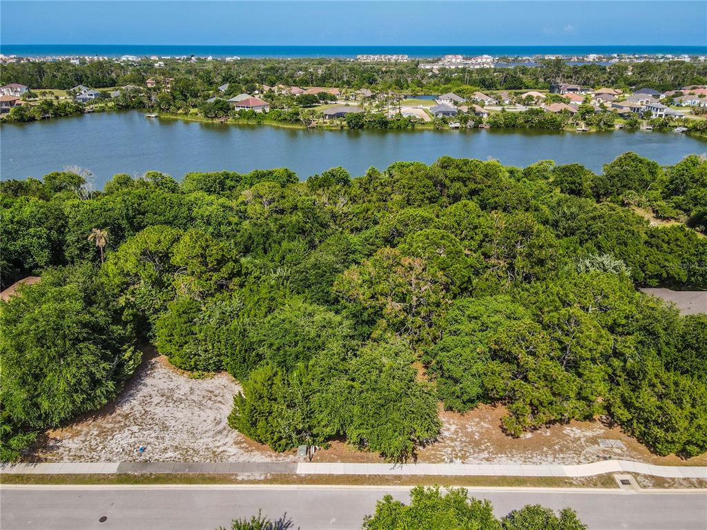 An aerial view shows a vacant, wooded lot bordering a lake with houses in the distance — 22 N LAKEWALK DRIVE, PALM COAST, FL