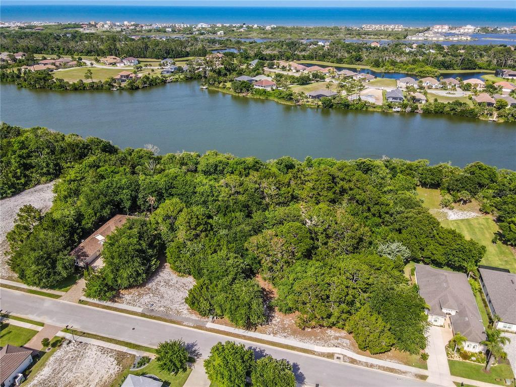 An aerial view shows a wooded vacant lot situated between two houses near a large lake — 22 N LAKEWALK DRIVE, PALM COAST, FL