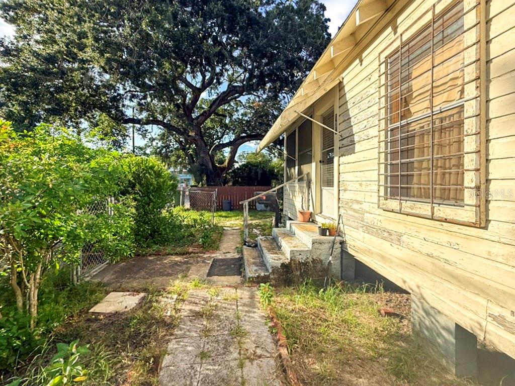 A side view of a weathered house with a concrete walkway, stairs, and large tree — 137 BLANCO STREET, ST AUGUSTINE, FL