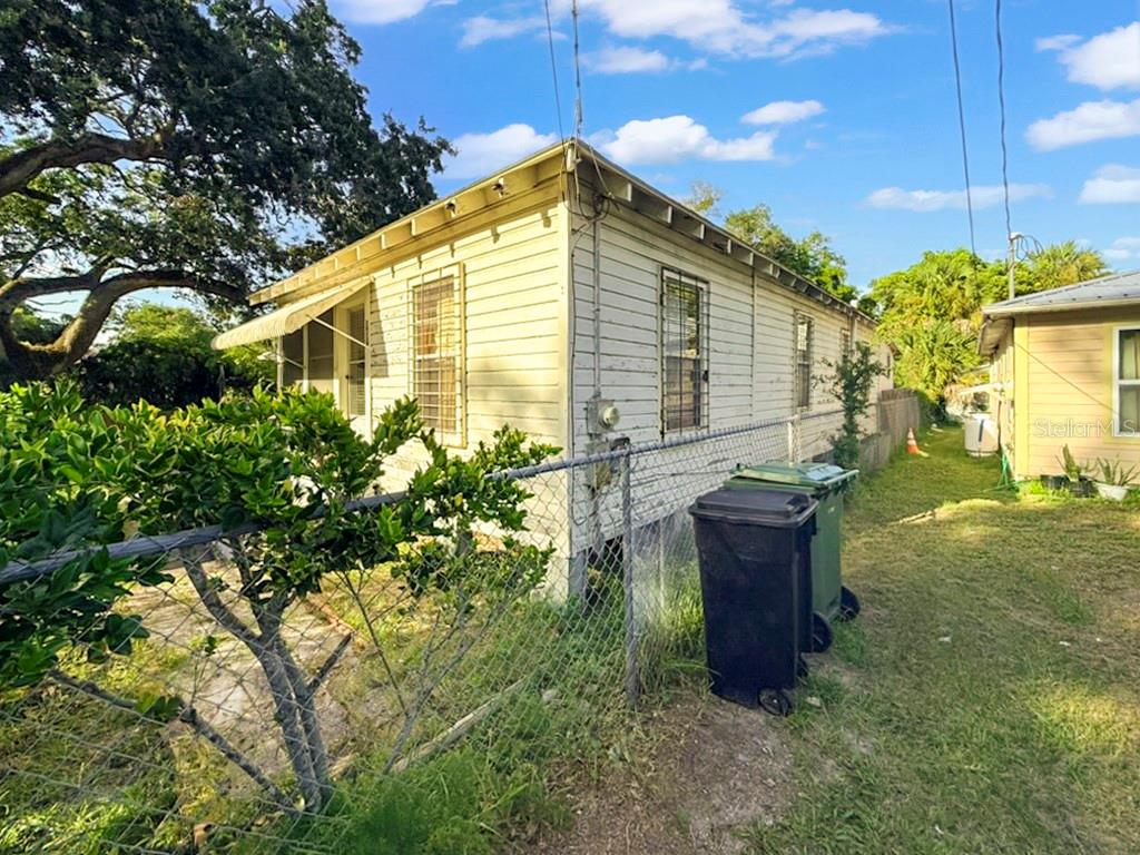 A white, single-story wood-sided house sits behind a chain-link fence with two trash bins outside — 137 BLANCO STREET, ST AUGUSTINE, FL