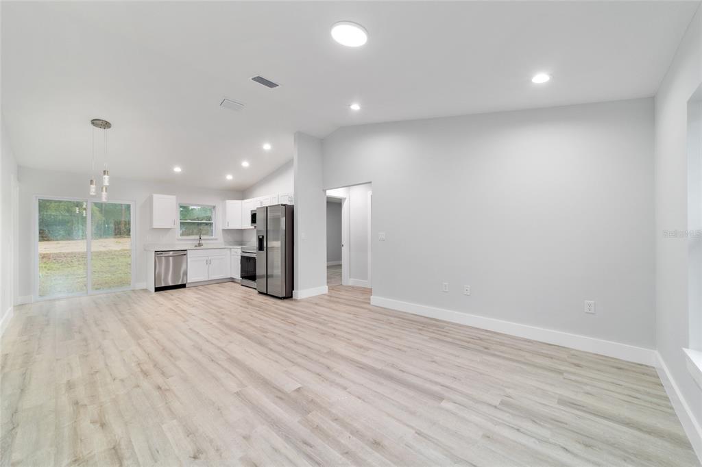 An open-concept kitchen and living area with gray walls, wood-look flooring, and sliding glass doors — 15776 SW 27TH LANE, OCALA, FL
