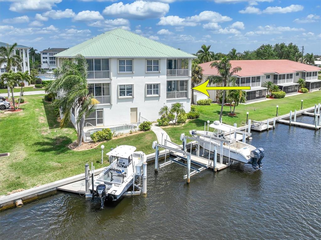 An aerial view of a multi-story waterfront building with boat docks and two boats — 129 BREAKERS COURT UNIT 121, PUNTA GORDA, FL