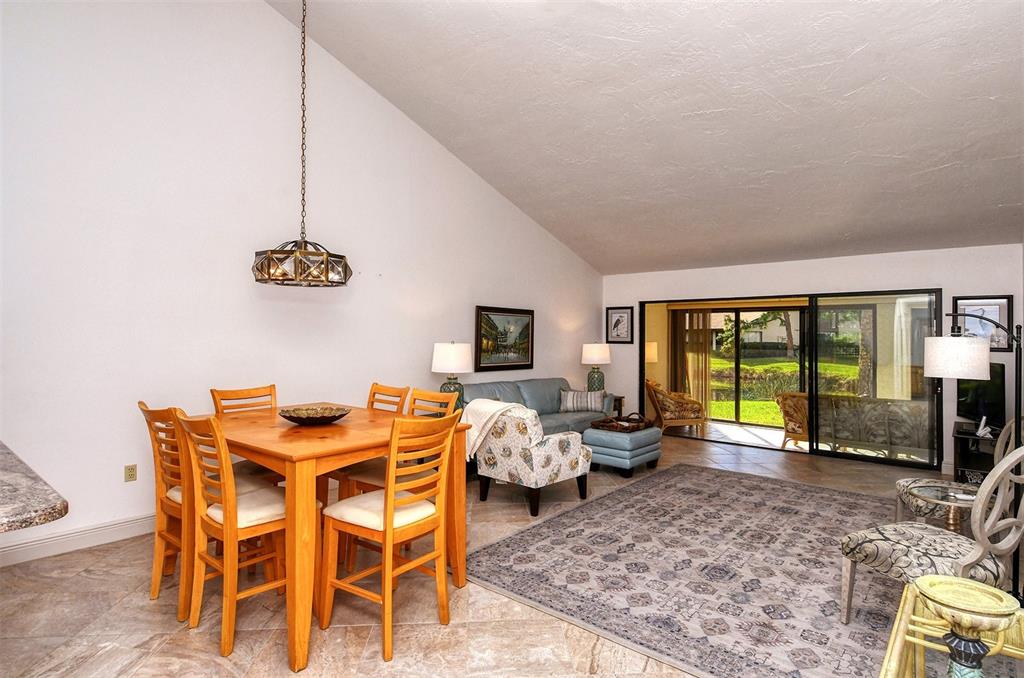 A dining area and living room with tile floors, vaulted ceilings, and sliding glass doors — 3131 WINDRUSH BOURNE UNIT 22, SARASOTA, FL