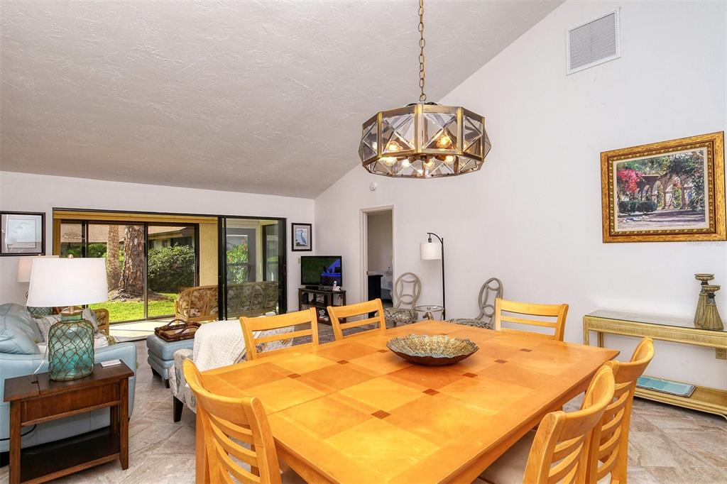 A dining area with a wooden table and chandelier opens to a living room and patio — 3131 WINDRUSH BOURNE UNIT 22, SARASOTA, FL