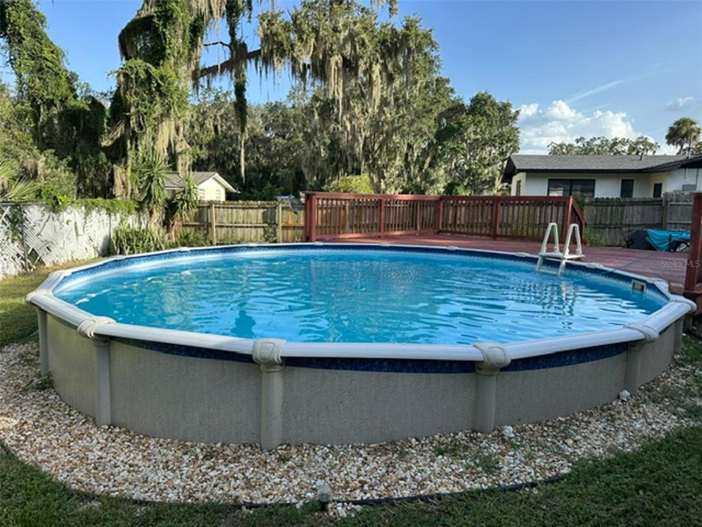 An above-ground swimming pool sits in a backyard with a wooden deck and gravel border — 1020 COTTONWOOD STREET, LEESBURG, FL