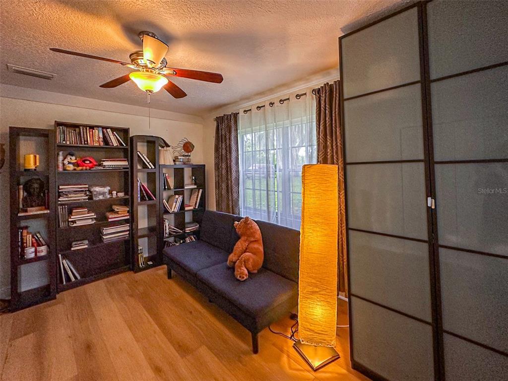 A room with wood flooring, a dark sofa, bookshelves, a floor lamp, and a ceiling fan — 1020 COTTONWOOD STREET, LEESBURG, FL