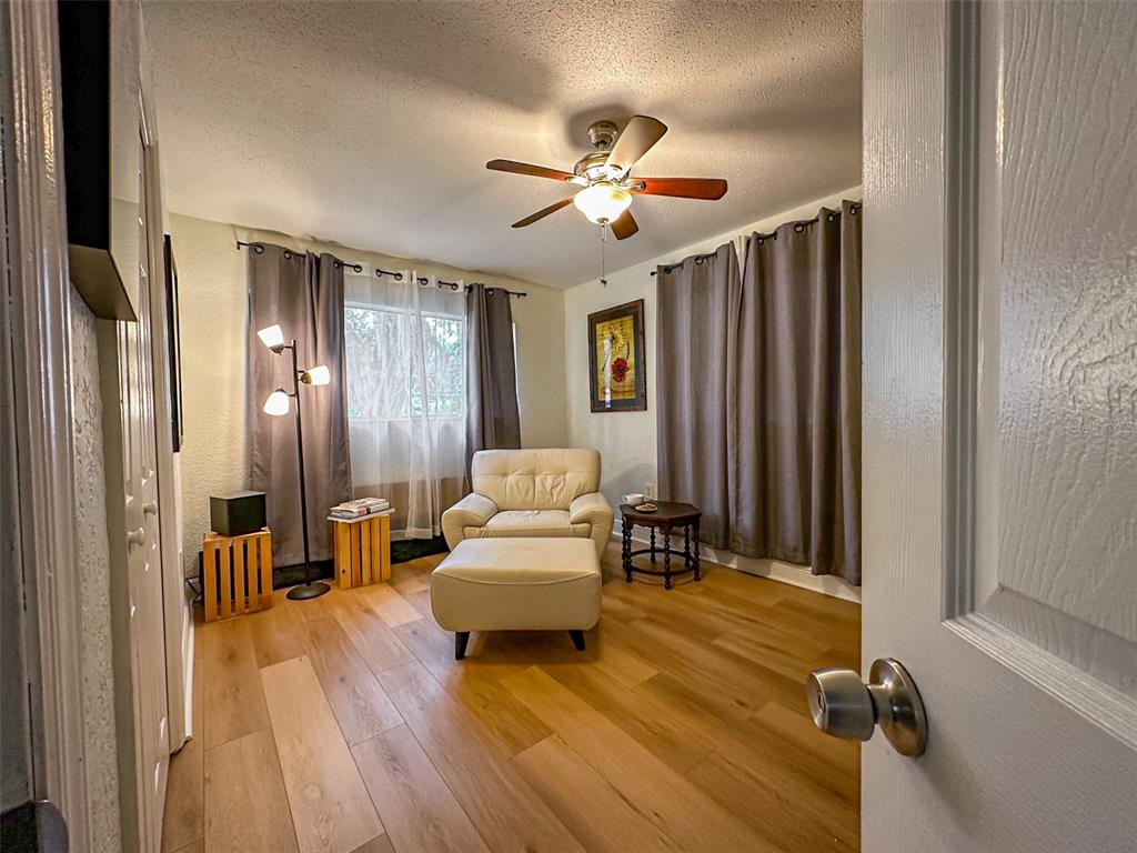 A small room features light wood flooring, a beige armchair with ottoman, and gray curtains — 1020 COTTONWOOD STREET, LEESBURG, FL
