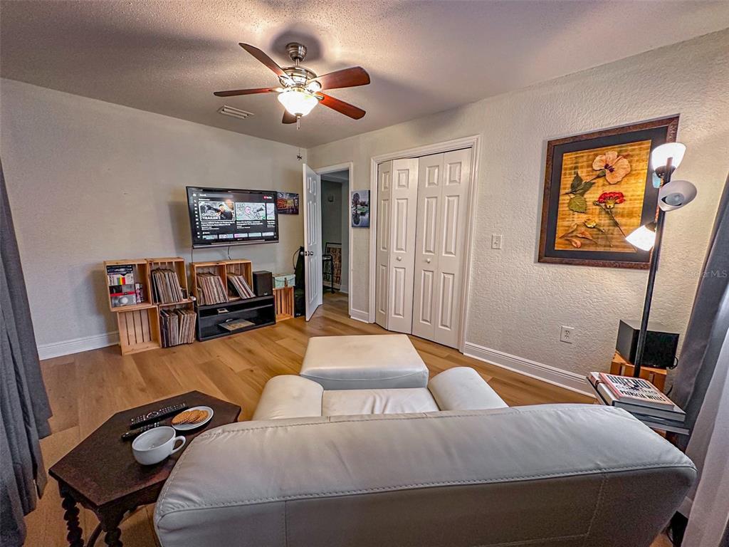 A living room features light wood flooring, a ceiling fan, a television, and white furniture — 1020 COTTONWOOD STREET, LEESBURG, FL