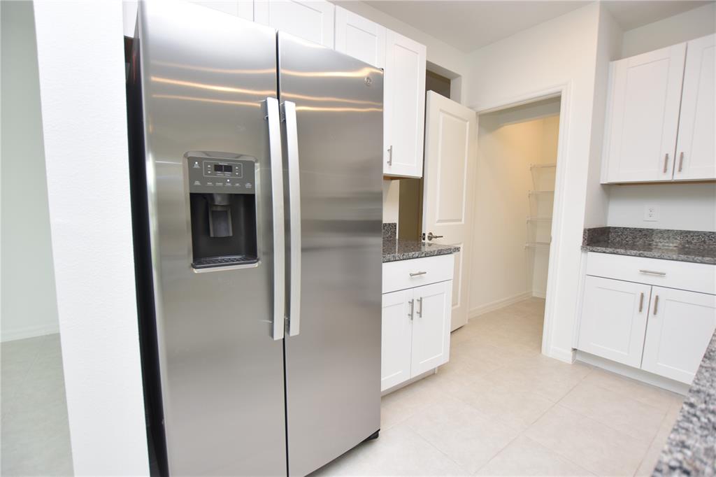 A kitchen features a stainless steel refrigerator, white cabinets, and granite countertops — 1855 RED LOOP, LAKELAND, FL