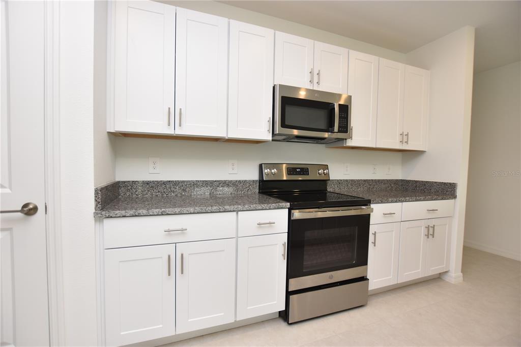 A kitchen features white cabinets, granite countertops, and stainless steel appliances — 1855 RED LOOP, LAKELAND, FL