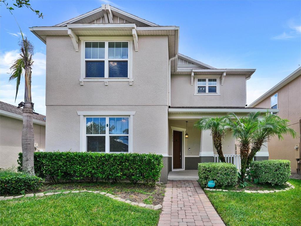 A two-story house with a beige stucco exterior, a front porch, and a landscaped yard — 14373 BREDA CENTER LOOP, WINTER GARDEN, FL