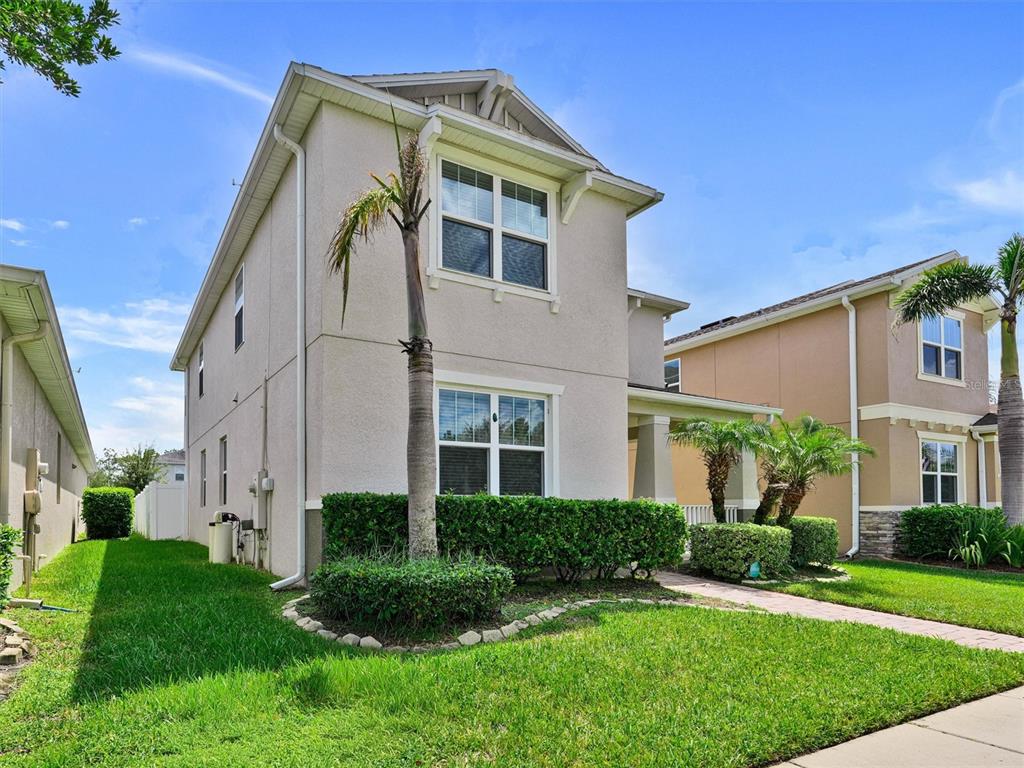 A two-story beige house with a palm tree, manicured hedges, and a paved walkway — 14373 BREDA CENTER LOOP, WINTER GARDEN, FL