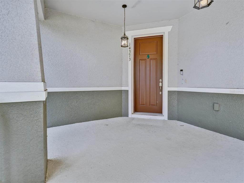 A covered entryway features a brown front door, light-colored concrete flooring, and two-toned exterior walls — 14373 BREDA CENTER LOOP, WINTER GARDEN, FL