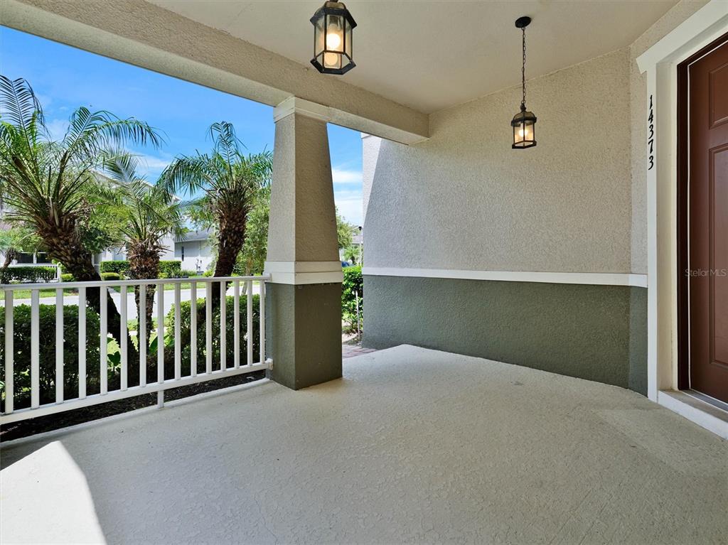 A covered front porch with a concrete floor, white railing, and two hanging lanterns — 14373 BREDA CENTER LOOP, WINTER GARDEN, FL