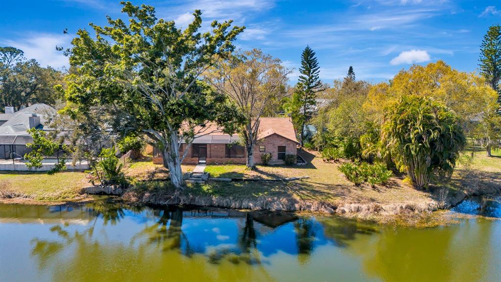 A single-story brick house sits on a grassy lot beside a calm lake — 5017 80TH AVENUE CIRCLE E, SARASOTA, FL