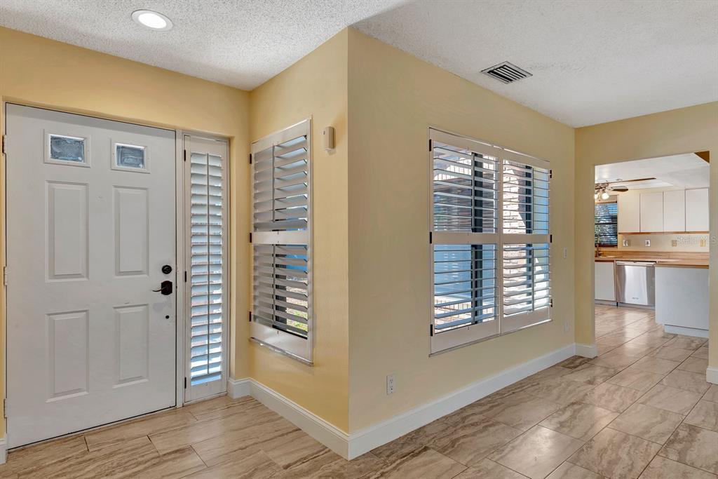 An entryway with tile flooring, a white front door, and plantation shutters on the windows — 5017 80TH AVENUE CIRCLE E, SARASOTA, FL