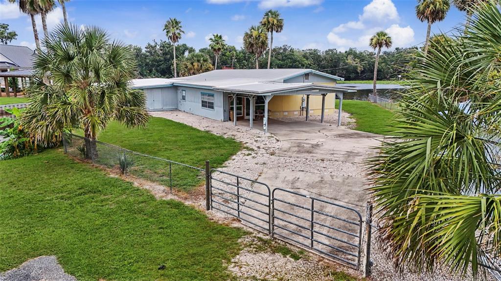A single-story house with a metal roof and carport sits on a grassy, fenced lot — 56440 WATER OAK ROAD, ASTOR, FL