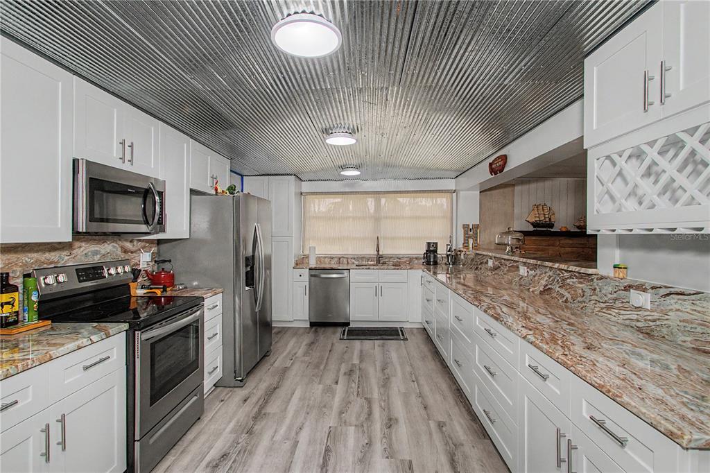 A kitchen features white cabinets, granite countertops, stainless steel appliances, and a corrugated metal ceiling — 56440 WATER OAK ROAD, ASTOR, FL