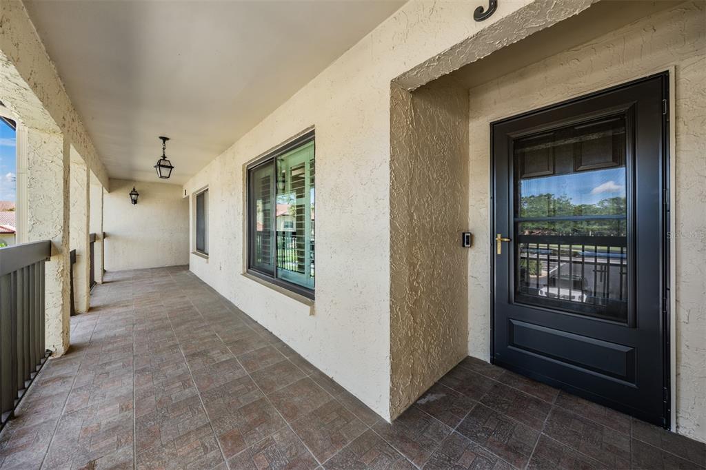 A covered balcony features tiled flooring, a dark door, and a large window — 1801 E LAKE ROAD UNIT 6J, PALM HARBOR, FL