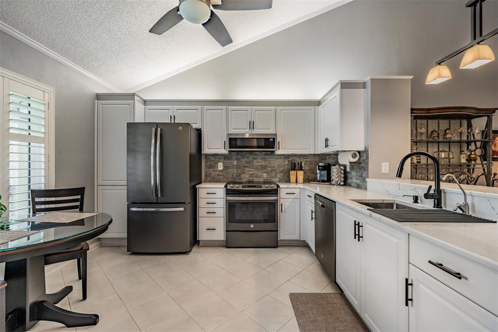 A kitchen with white cabinets, stainless steel appliances, a gray tile backsplash, and tile flooring — 1801 E LAKE ROAD UNIT 6J, PALM HARBOR, FL