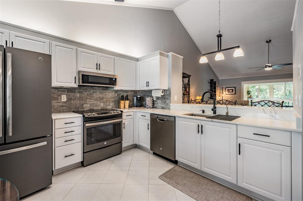 A kitchen with white cabinets, stainless steel appliances, gray tile backsplash, and white countertops — 1801 E LAKE ROAD UNIT 6J, PALM HARBOR, FL