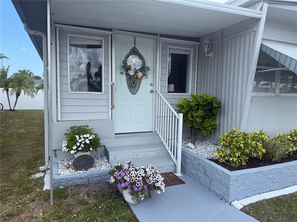 The exterior of a mobile home features a white front door, steps, and landscaping — 6190 DAFFODIL ROAD, VENICE, FL