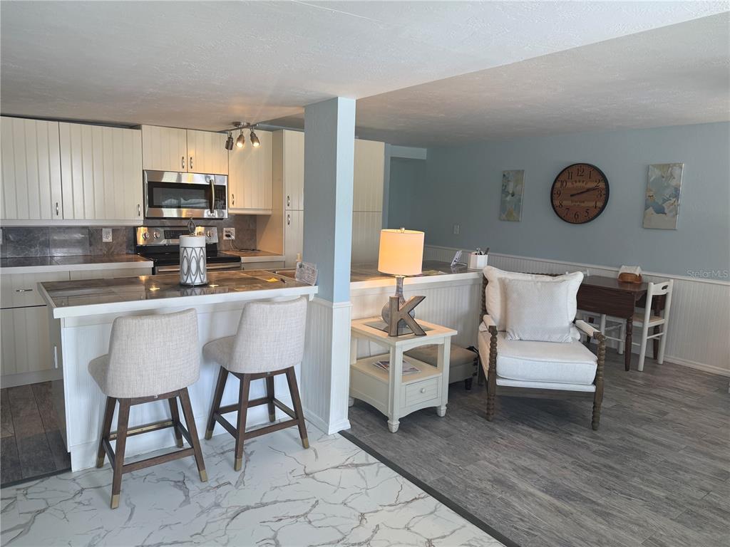 A kitchen with white cabinets and a breakfast bar opens into a living area — 6190 DAFFODIL ROAD, VENICE, FL