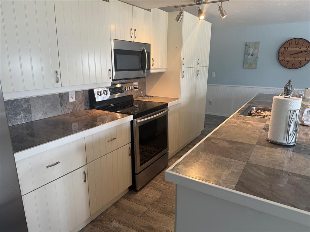 A kitchen features white beadboard cabinetry, dark stone countertops, stainless steel appliances, and tile flooring — 6190 DAFFODIL ROAD, VENICE, FL