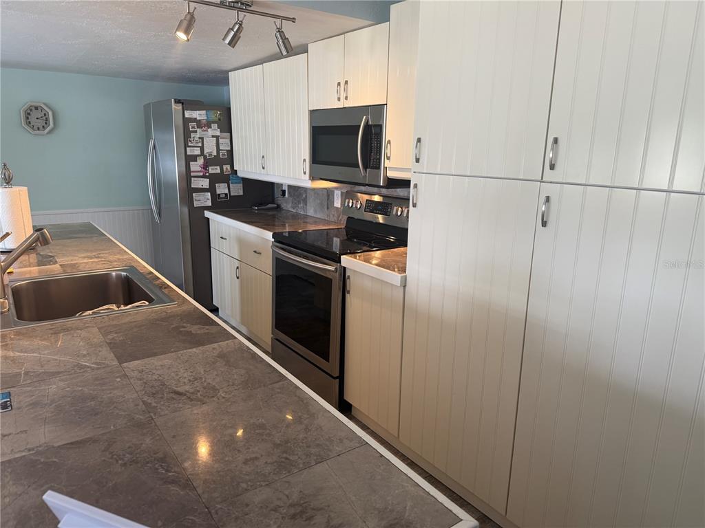 A kitchen features white beadboard cabinetry, stainless steel appliances, and dark stone tile countertops — 6190 DAFFODIL ROAD, VENICE, FL