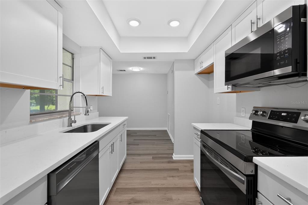 A galley kitchen features white cabinets, stainless steel appliances, quartz countertops, and wood-look flooring — 837 WESTPORT DRIVE, ROCKLEDGE, FL