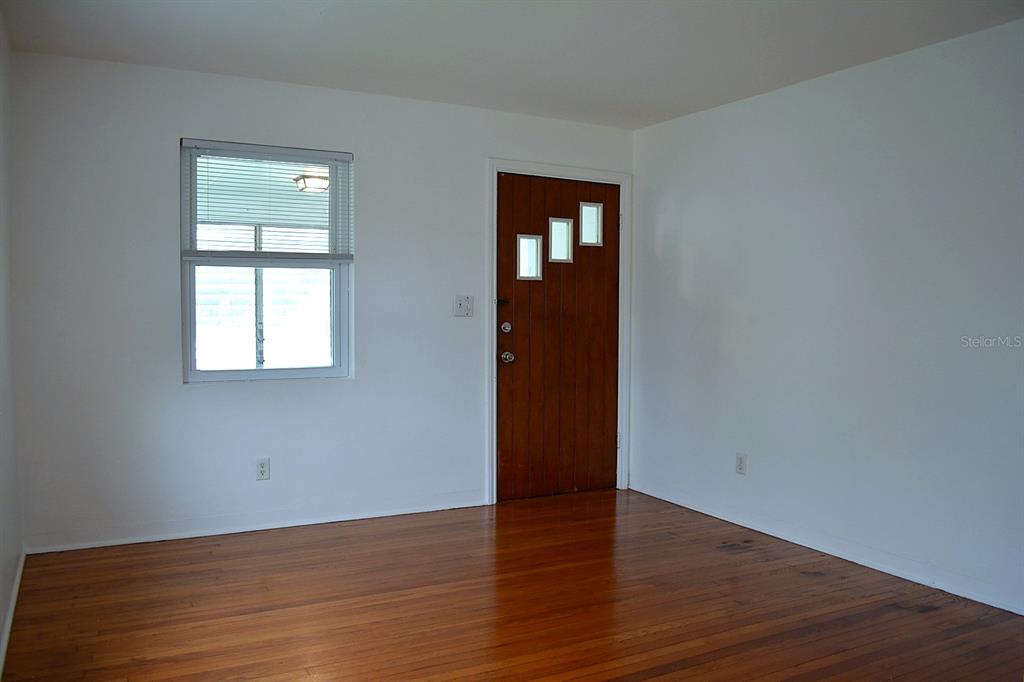 An empty room features white walls, hardwood flooring, a single window, and a wooden door — 1401 34TH AVENUE N, ST PETERSBURG, FL