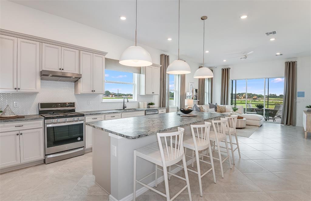 A kitchen with light gray cabinets, a granite island, and white bar stools faces a living area — 6323 DEW DROP LOOP, ST CLOUD, FL