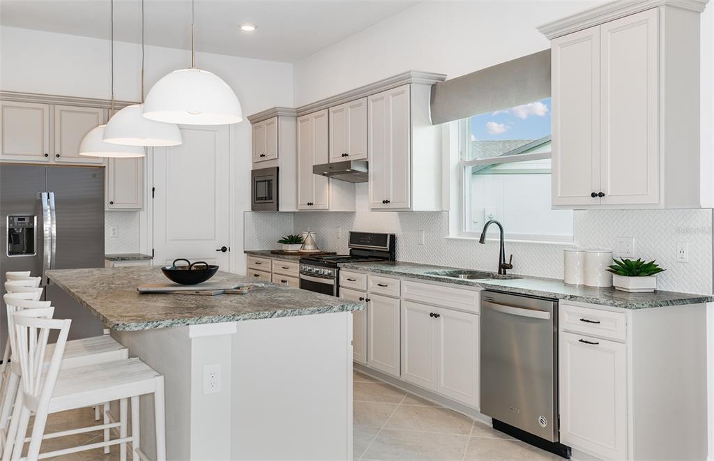 A modern kitchen features white cabinetry, granite countertops, stainless steel appliances, and a central island — 6323 DEW DROP LOOP, ST CLOUD, FL