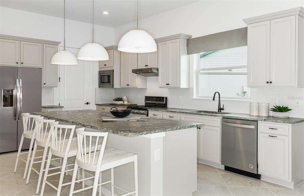A kitchen features white cabinets, granite countertops, a large island, and stainless steel appliances — 6323 DEW DROP LOOP, ST CLOUD, FL