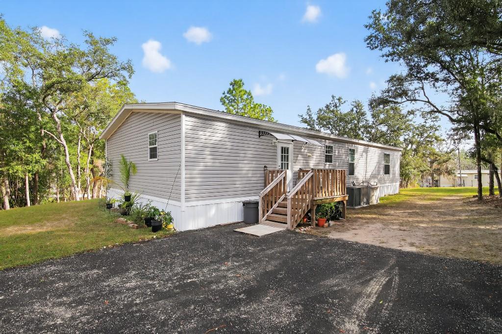 A single-story manufactured home with grey vinyl siding, a wooden deck, and a paved driveway — 13230 NE 9TH STREET, WILLISTON, FL