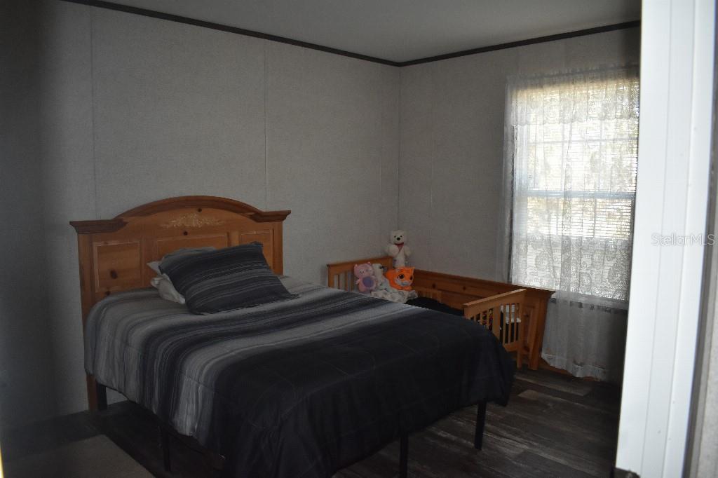 A bedroom features a wooden bed frame, gray wood-look flooring, and a window with curtains — 13230 NE 9TH STREET, WILLISTON, FL