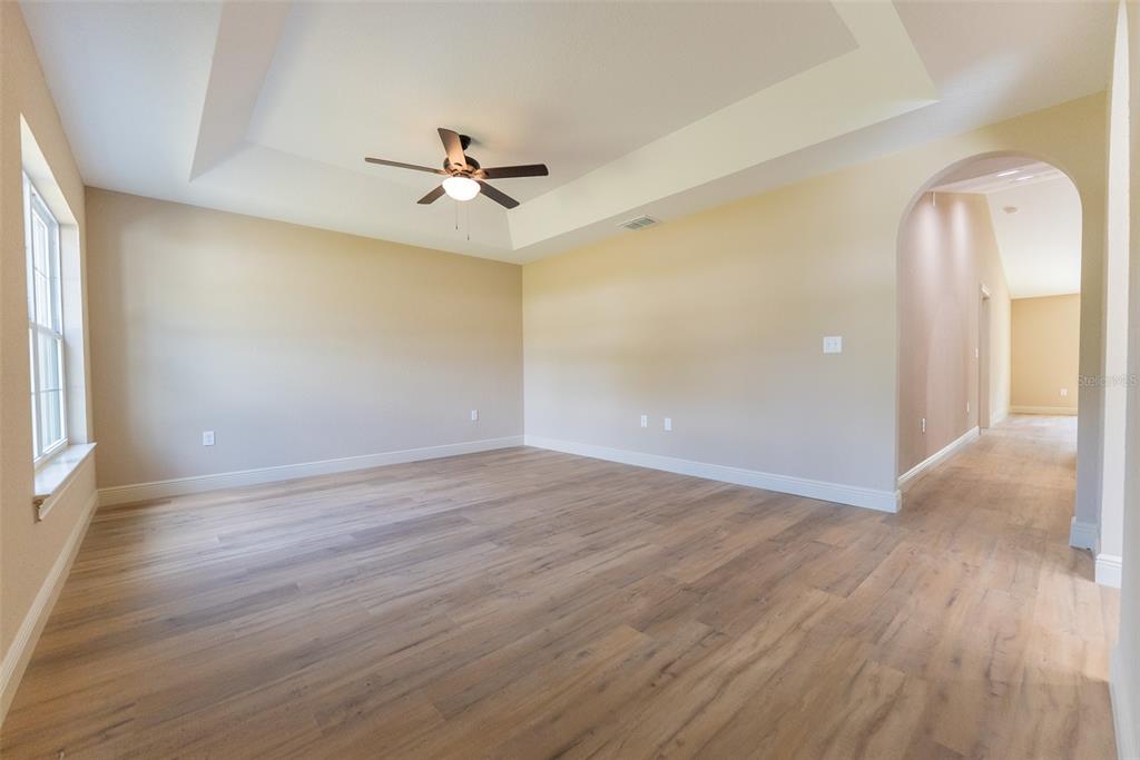 An empty room with light wood flooring, a tray ceiling, and an arched entryway — 3250 SW WESTWATER DRIVE, DUNNELLON, FL