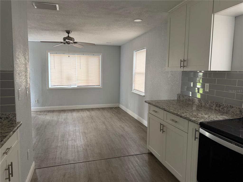 A kitchen with white cabinets and granite countertops opens into a living area with wood flooring — 4735 21ST AVENUE N, ST PETERSBURG, FL