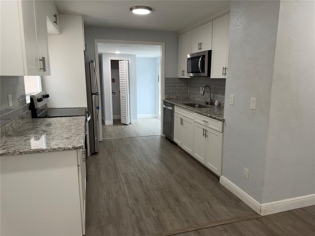 A kitchen features white cabinets, granite countertops, stainless steel appliances, and gray wood-look flooring — 4735 21ST AVENUE N, ST PETERSBURG, FL