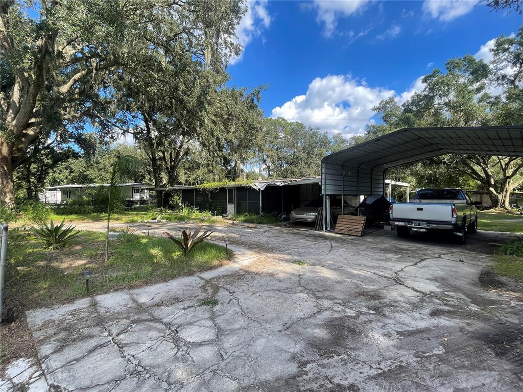 A single-story home with a metal carport and a cracked concrete driveway under large trees — 840 & 846 NASHVILLE ROAD, LAKELAND, FL