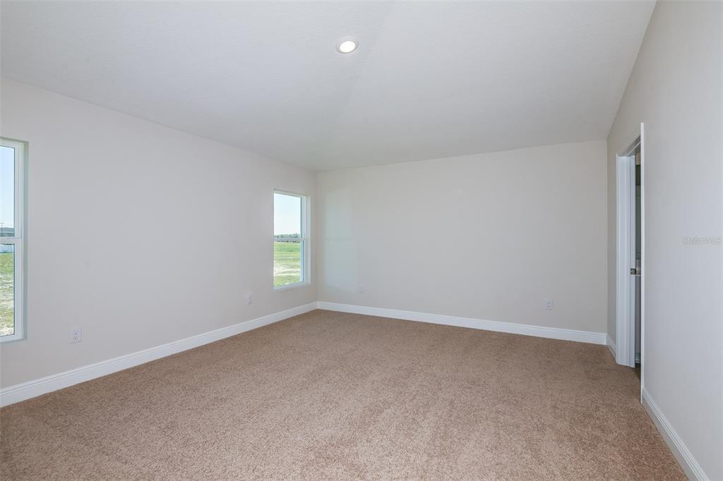 An empty bedroom features beige carpet, neutral walls, two windows, and a doorway — 6085 SW 96TH PLACE, OCALA, FL