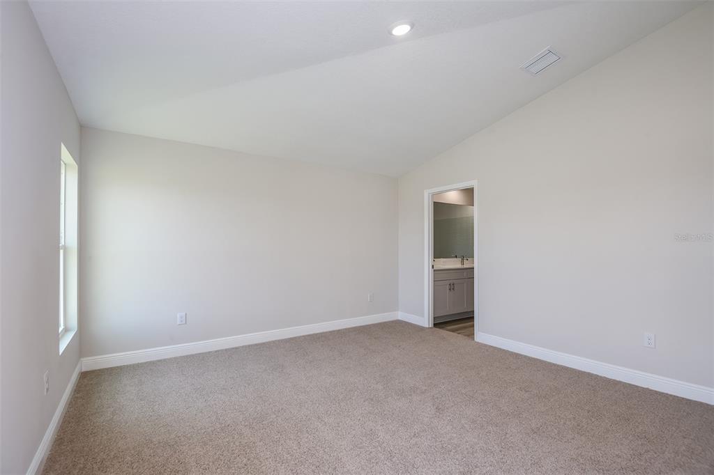 An empty bedroom features beige carpet, light-colored walls, a vaulted ceiling, and an attached bathroom — 6085 SW 96TH PLACE, OCALA, FL