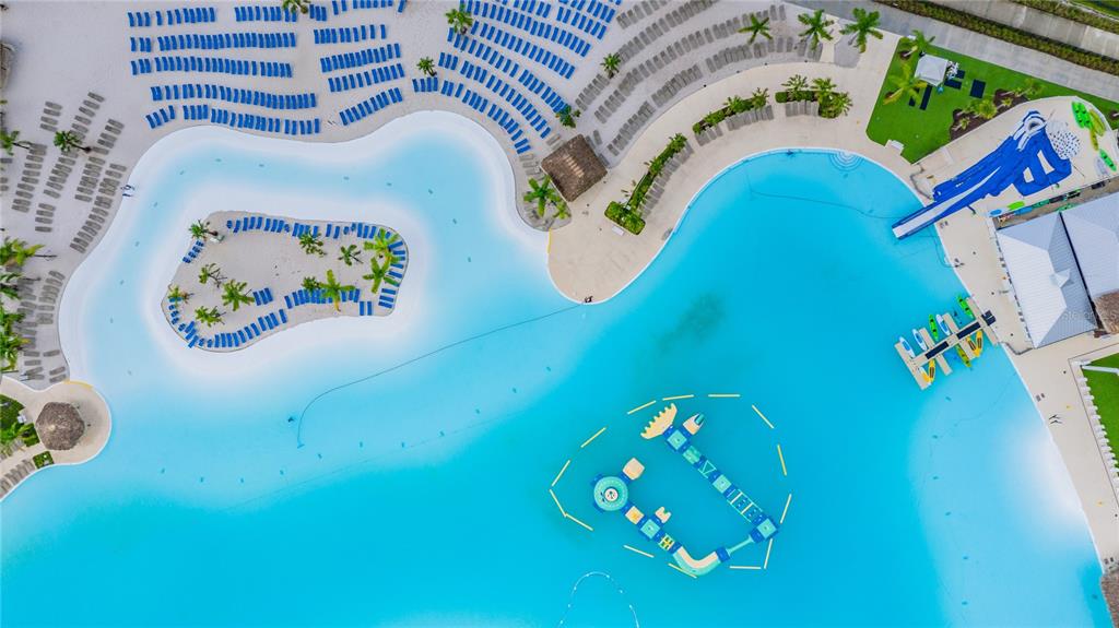 An aerial view shows a large swimming lagoon with an island, water slide, and lounge chairs — 31486 TANSY BEND, WESLEY CHAPEL, FL