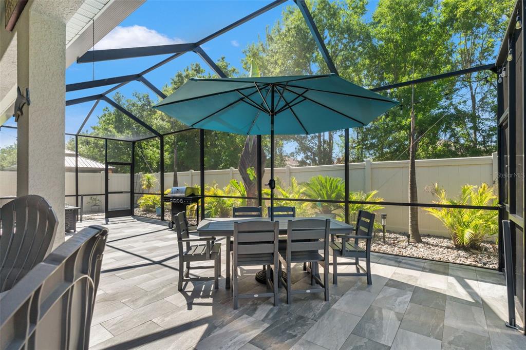 A screened-in patio features gray tile flooring, a dining set with an umbrella, and landscaping — 31486 TANSY BEND, WESLEY CHAPEL, FL