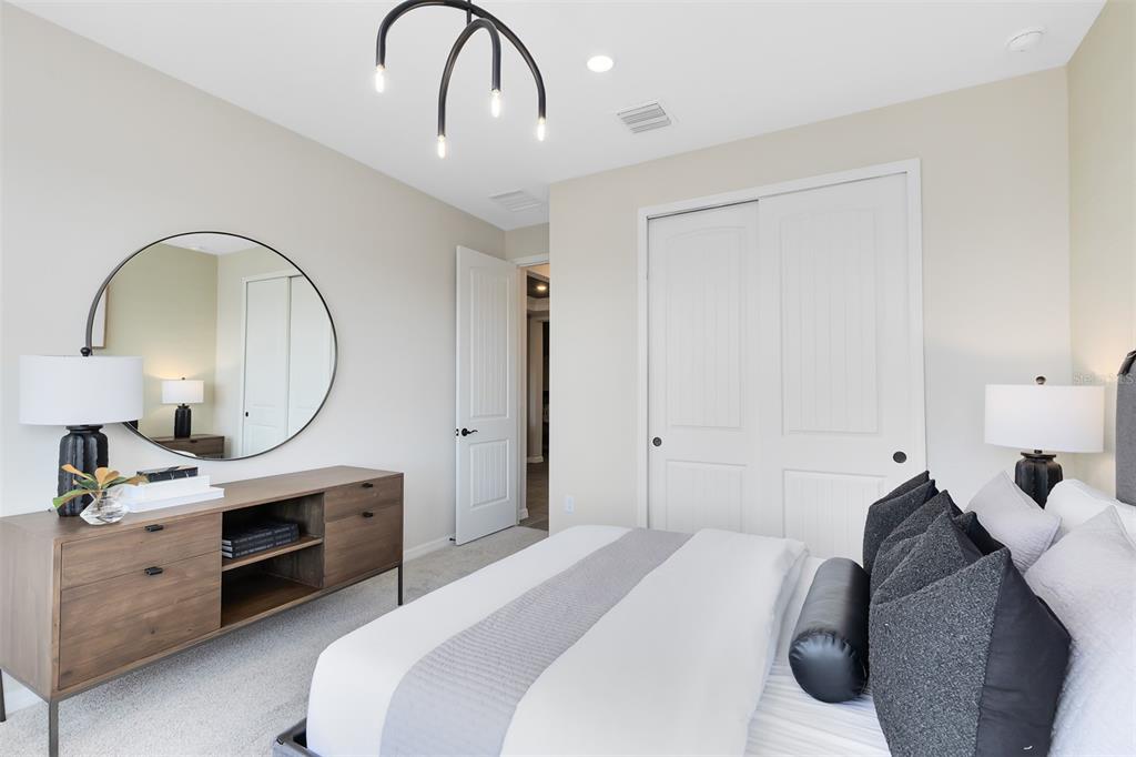 A bedroom features a bed, a wooden dresser with a round mirror, and sliding closet doors — 5679 FLAME VINE WAY, ST CLOUD, FL