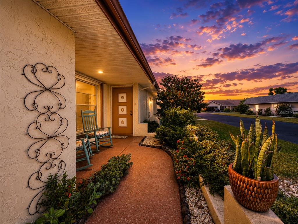 A front porch with two rocking chairs, a decorative metal wall trellis, and landscaping at sunset — 310 FAIRCROSS CIRCLE, SUN CITY CENTER, FL